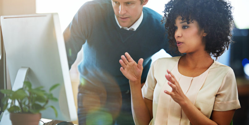 Shot of adults talking together at a workstation in an